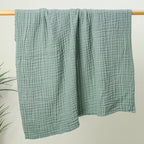 Sage green 6-layer cotton muslin throw hanging on a rail