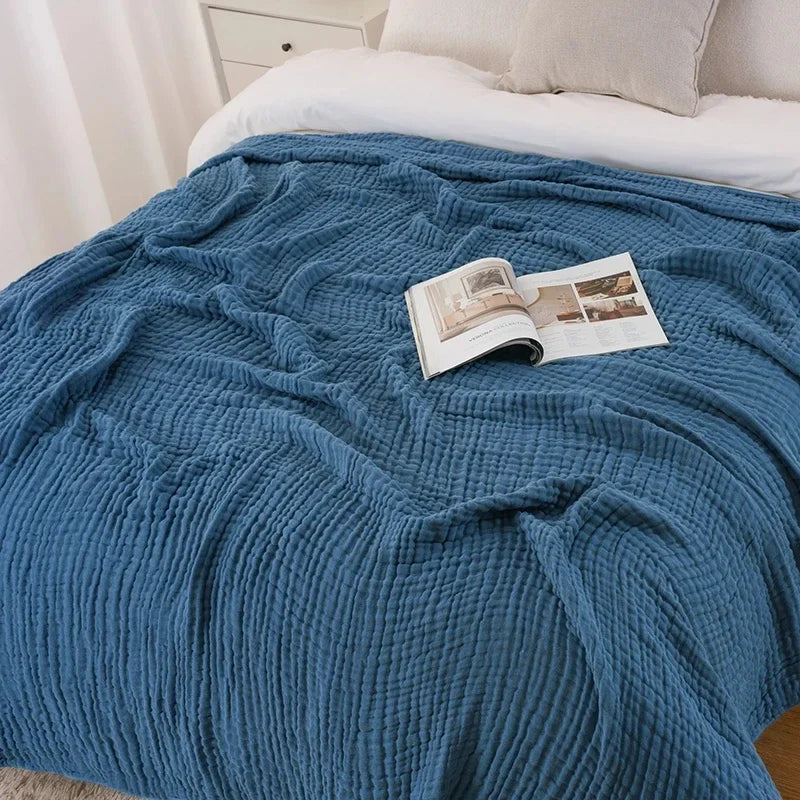 Navy blue cotton muslin blanket on a bed with a magazine
