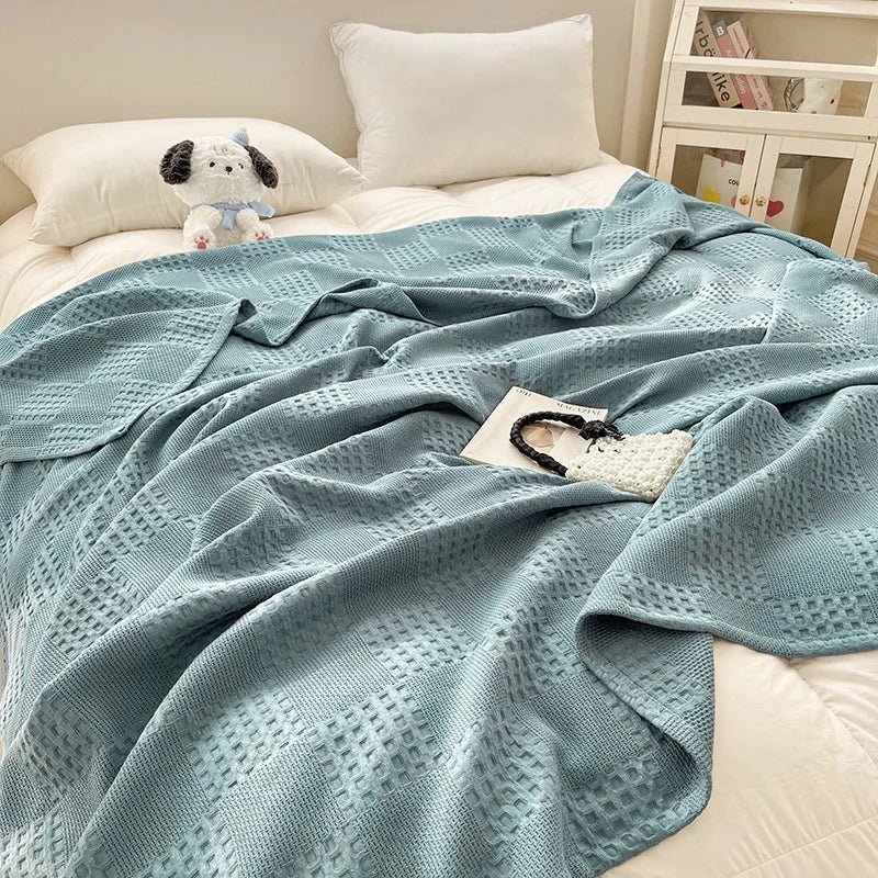 Dusty blue cotton waffle weave blanket draped on a bed