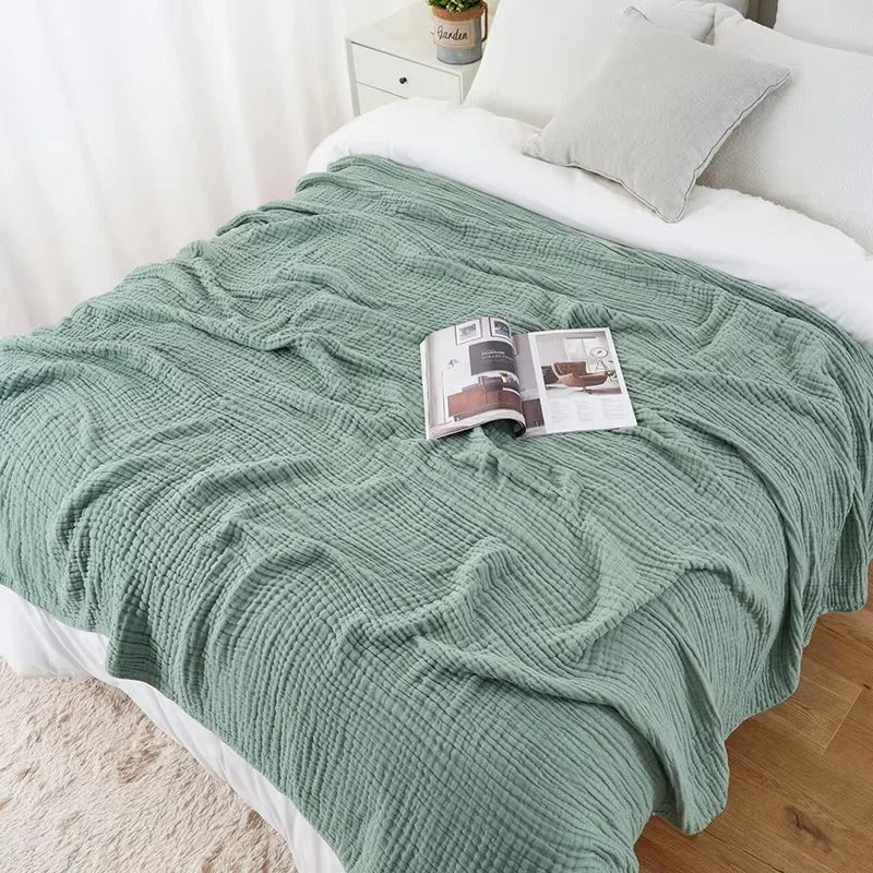 Sage green cotton muslin blanket on a bed with an open magazine